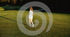 A young female golfer is walking along the golf course. Back view