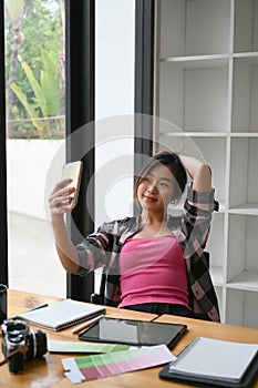 Young female graphic designer taking a selfie on her smart phone a her workplace.