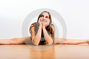 Young female gymnast rests on the floor with a dreamy face while practicing a split