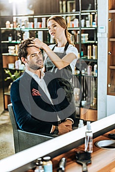 Young female hairdresser doing hairstyle to handsome man