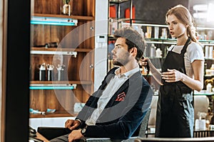 Young female hairdresser holding hair dryer and looking at handsome male client