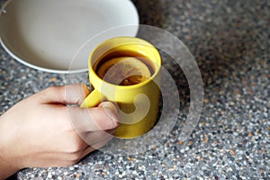 Young female hand holding a yellow cup with tea, honey and lemon slice