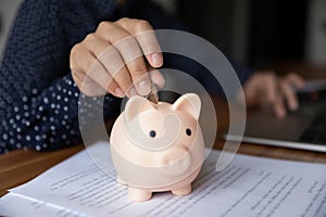 Young female hand putting coin to piggybank, rational economy concept