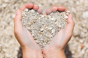 Young female hands hold small pebble stones in heart shape.