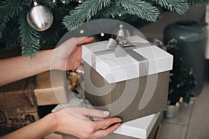 Young female hands holding gift box near the Christmas tree. New Year atmosphere