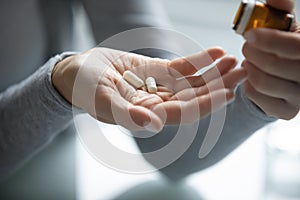 Young female hands holding opened pill bottle and two capsules