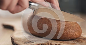 Young female hands slicing rye wheat rustic bread on cutting board