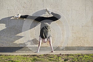 Young female handstand against the wall performs acrobatic elements