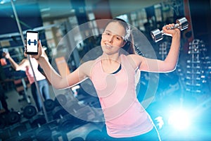 Young female has personal online workout or exercising with dumbbells in gym
