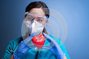 young female healthcare worker in mask and goggles, holding a heart