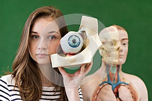 Young female high school student holding human eye model. Student in Biology class