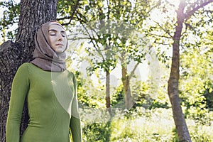 Young female in a hijab and casual clothes in the park. Protecting the environment and caring for plants concept