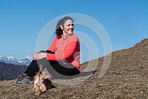 Young female hiker sitting with her dog on hill slope and looking over shoulder