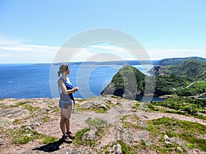 A young female hiker standing above the atlantic ocean overlooking Quidi Vidi and the rugged coast of Newfoundland and Labrador