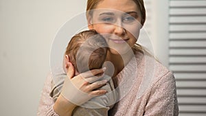 Young female holding healthy newborn baby in arms, loving and tender mommy