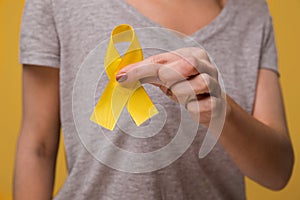 Young female holding yellow gold ribbon awareness symbol for endometriosis, suicide prevention, sarcoma bone cancer