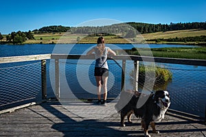 Young female holidaymaker with her dog  on wooden jetty over lake with blue skys enjoying her holiday.lozere france
