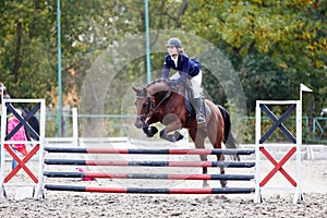 Young female horse rider jumping over the obstacle on equestrian competition