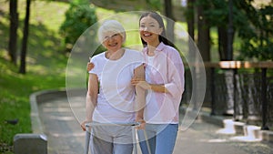 Young female hugging elderly woman with walking frame outdoors, rehabilitation