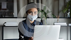 Young female indian professional in facemask working on computer.