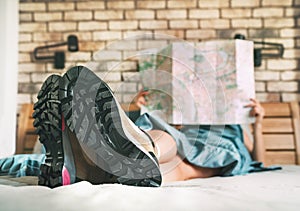 Young female inspecting a city map resting on the bed under the blanket weared trekking boots on bed sheets. Boot sole close up