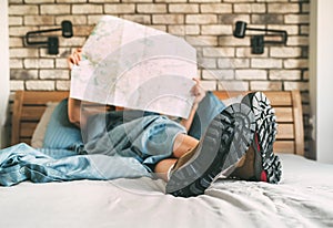 Young female inspecting a city map resting on the bed under the blanket weared trekking boots on bed sheets. Boot sole close up photo