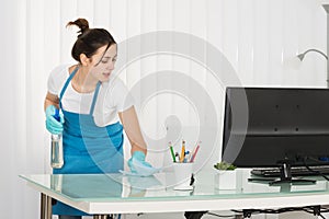 Young Female Janitor Cleaning Desk With Rag