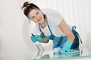 Young Female Janitor Cleaning Desk With Rag