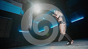 A young female kickboxer kicking a black punching bag with a powerful kick. Athlete practicing attack exercises in a