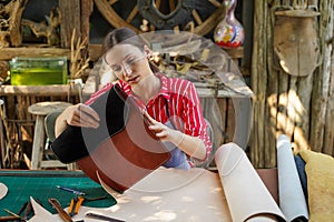 Young female leather goods maker looking and check the neatness of the leathers bag before sell to customer in workshop