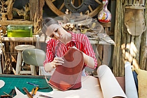 Young female leather goods maker looking and check the neatness of the leathers bag before sell to customer in workshop photo