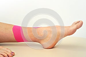 Young female leg and feet with pink kinesiology tape applied closeup detail