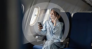 Young female listening song during flight in first class cabin using smartphone, woman entertain on airplane board enjoy