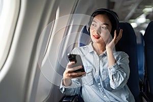 Young female listening song during flight in first class cabin using smartphone, woman entertain on airplane board enjoy