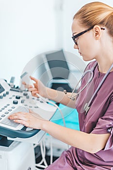 Young female londe doctor with black glasses. Ultrasound scanner in the hands of a doctor. Diagnostics. Sonography