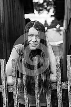 Young female with long hair, portrait, standing near the wooden fence in the village.