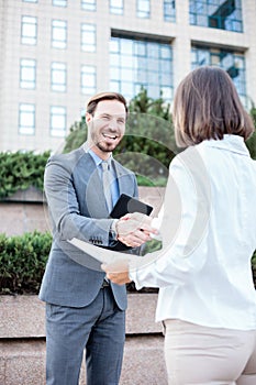 Young female and male business people shaking hands after a successful meeting in front of an office building