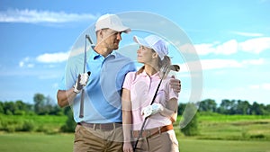 Young female and male with golf clubs hugging and smiling each other sport study