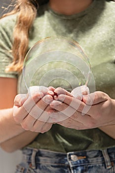 Young female and male hands holding a big soap bubble on an out of focus background. Couples and fun concept