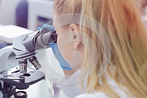 Young female male scientist looking through a microscope in a laboratory doing research, microbiological analysis, medicine