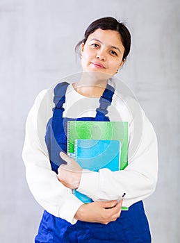 Young female mechanic in blue overalls holding workbooks