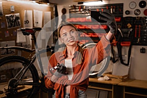 Young female Mechanic in a workshop takes a selfie after finished working on a repair bicycle