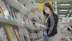 Young female in medical mask buying journal in supermarket