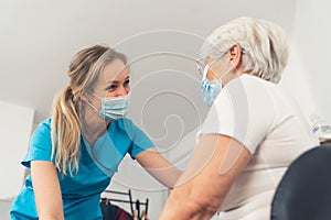 A young female medical professional, wearing a blue uniform and a face mask, having a pleasant conversation with her