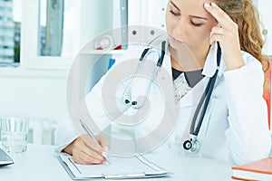 Young female medicine doctor writing something on clipboard closeup. Physician ready to examine patient.