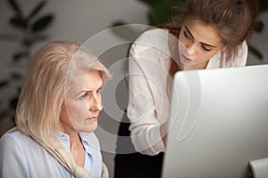 Young female mentor teaching senior woman colleague explaining c