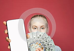 Young female model showing smartphone with blank empty white screen display and money cash us dollars on bright red background