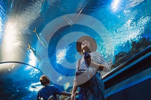 Young female with modern photo camera walking in indoor huge aquarium tunnel, enjoying a underwater sea inhabitants. Around the