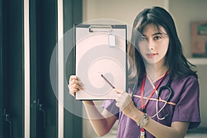 Young female nurse holding pencil and showing her clipboard