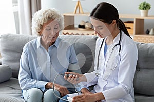 Young female nurse measure blood pressure check old grandma patient